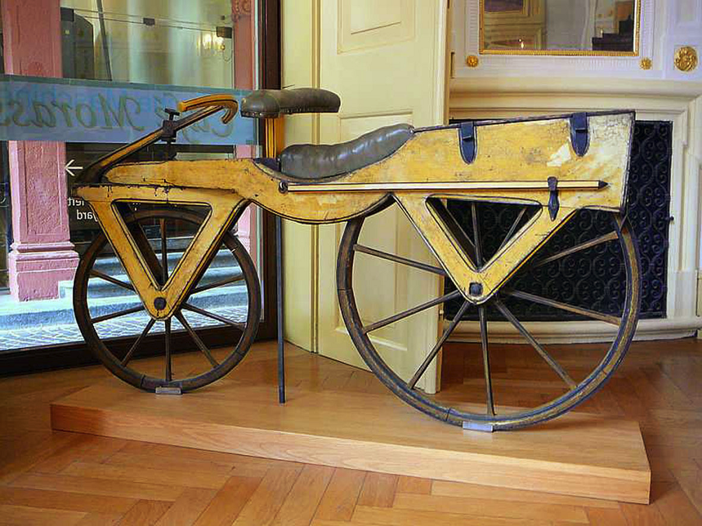 На фото – первый велосипед, у него даже педалей нет. Изобретен в 1818 году бароном Карлом фон Дрейзом
